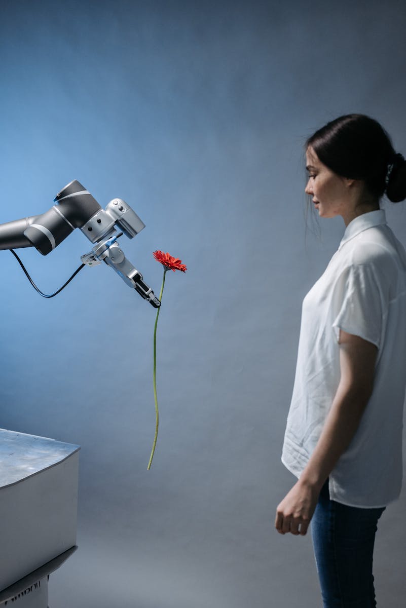 A woman observes a robot holding a red flower, symbolizing technology and nature integration.